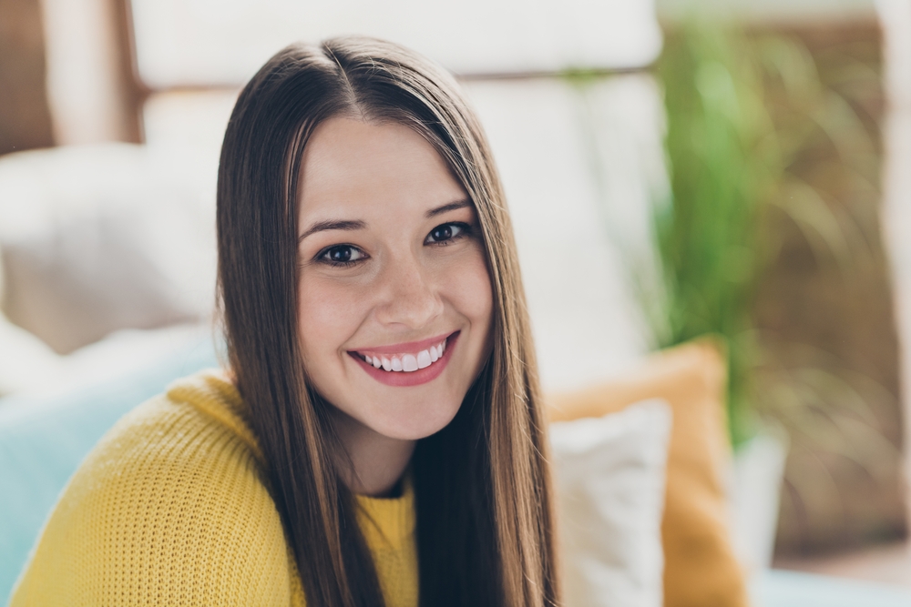 A smiling woman with long brown hair wearing a yellow sweater