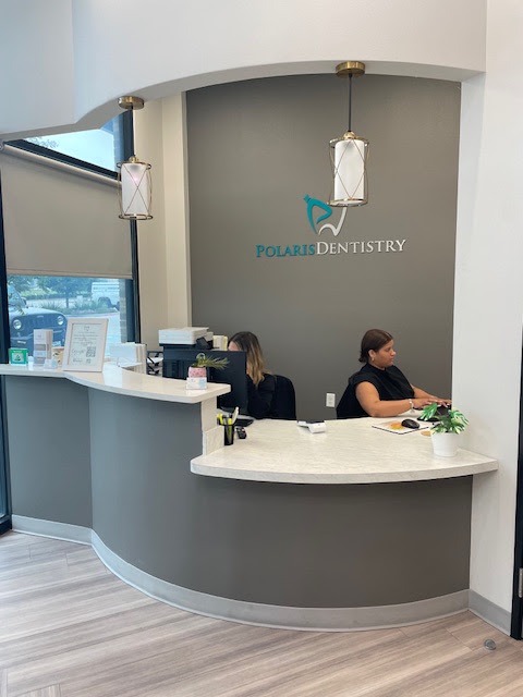 Two team members behind the curved reception desk beneath the Polaris Dentistry logo
