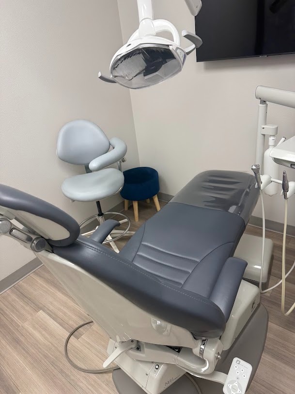 Dental treatment room with a reclining chair, overhead examination light, and wall-mounted TV