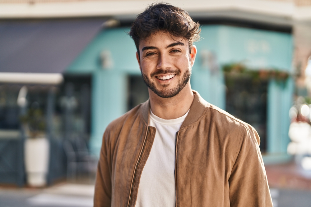 A smiling man in a tan jacket standing outdoors