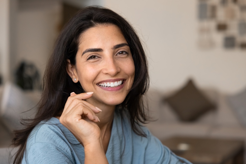 A smiling woman with dark hair wearing a blue shirt at home
